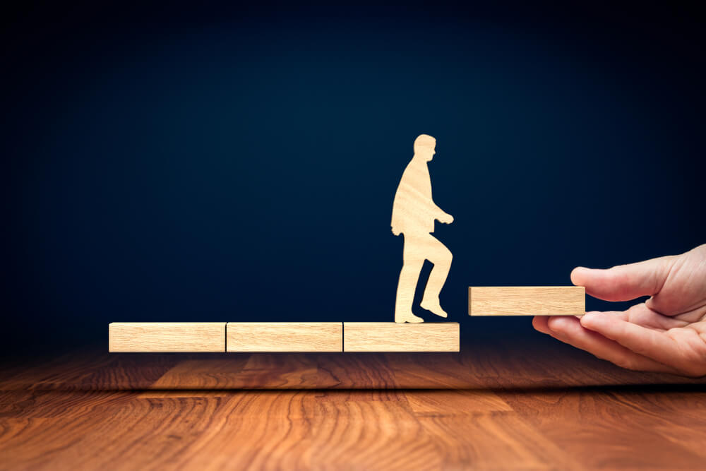 wooden figure stepping on singular elevated wooden block, mentoring concept
